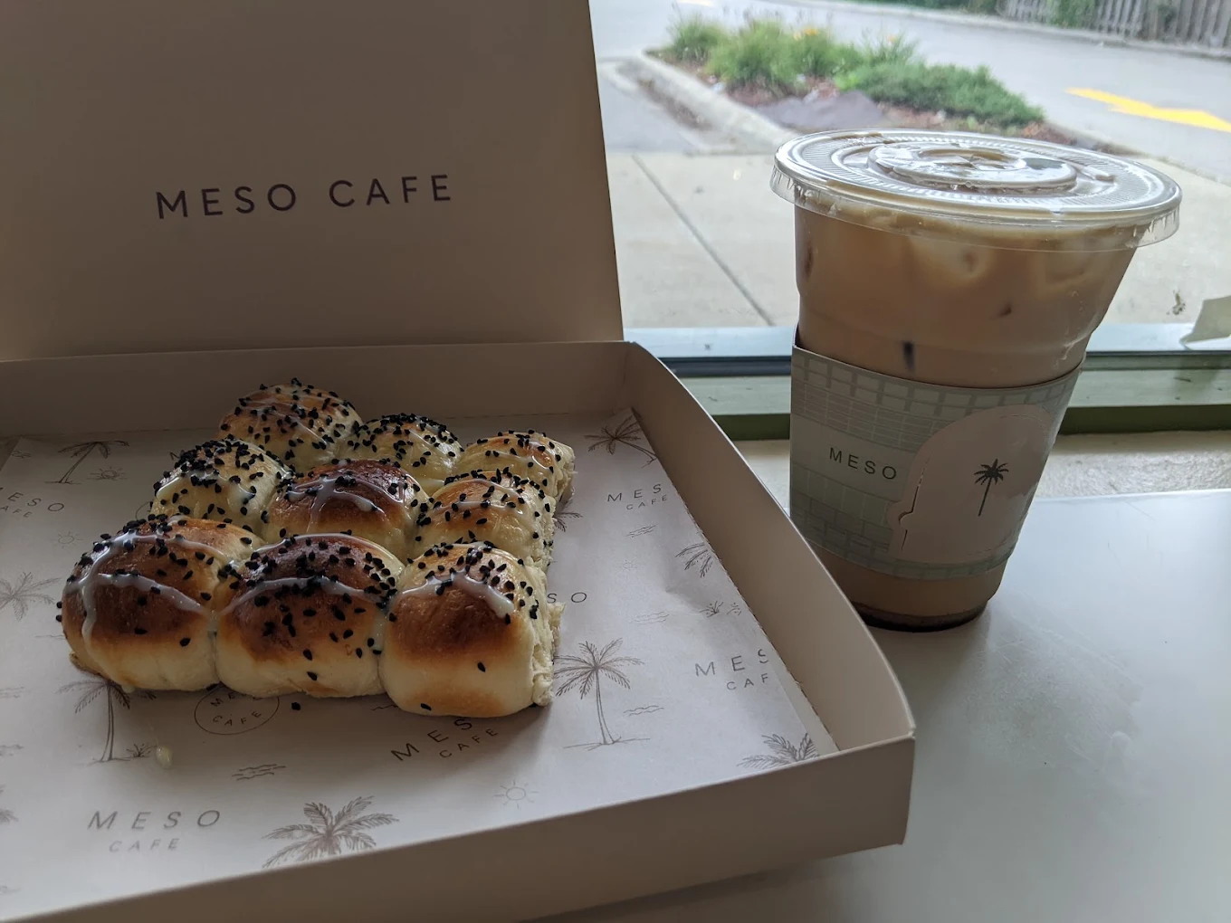 A box of sesame rolls and an iced latte on the window ledge