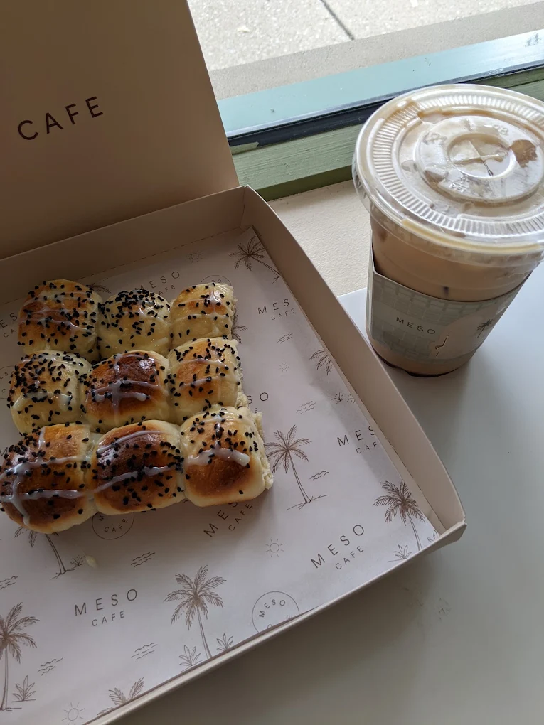 An iced latte in a Meso Cafe sleeve beside a box of sesame-topped rolls