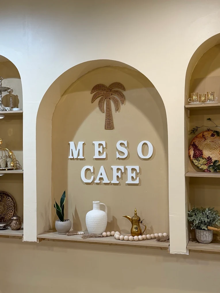 The Meso Cafe sign in an arched alcove, with a brass dallah and a rattan palm